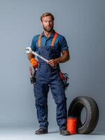 Professional Mechanic Posing with Tools and Tire in Overalls photo