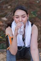 A woman is drinking water while sitting on a bench photo