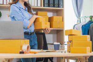 Asian woman starts small SME business using her home as Home Office and checks inventory to ensure that there are enough items to deliver to customers according to orders. Small SME Business Startup photo
