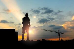 Silhouette of Engineer on building site, construction site at sunset in evening time photo