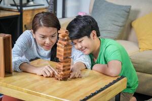 Mother and Son Playing Block Game at Home, Happy Asian Family Bonding with Fun Indoor Game, Parent and Child Enjoying Quality Time Together photo