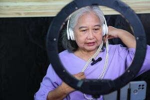 Senior Asian Woman Creating Jewelry for Online Selling and Online Tutorial, Senior Woman Creating Online Content Live Streaming or Vlogging from Home photo
