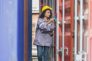 Female engineer in the hard hat uses digital tablet inspecting container box in industry cargo photo