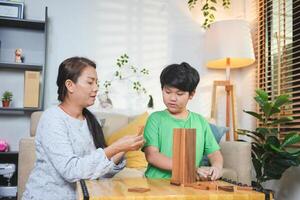 Mother and Son Playing Block Game in Living Room at Home, Happy Asian Family Bonding with Fun Indoor Game, Parent and Child Enjoying Quality Time Together photo