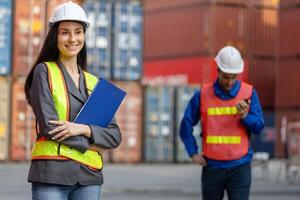 Female engineer with clipboard inspecting containers box at shipping yard, Caucasian woman working in industry containers cargo standing with blurred worker in background photo