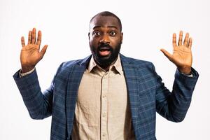 Studio photo of serious African male manager showing shock and surprise while standing in front of gray background.