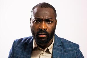 Portrait of an angry African-American businessman in a suit, looking directly at the camera with a frustrated expression against a gray studio background. photo
