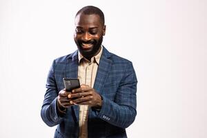 Studio shot of black businessman with a joyful expression, laughing while using his phone for text messaging. photo