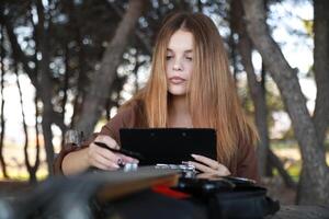 Girl Writes Music Notes On Sheet Music At The Park Table In The Nature photo