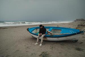 Man Reading A Book Sitting On The Beach In Winter Near A Boat photo