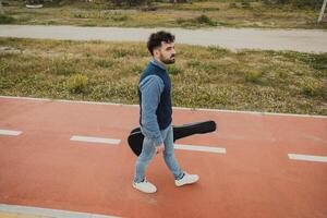Musician With Guitar Case Walking On The Sidewalk Near The Sea photo