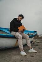 Man Carefully Reads A Book While Relaxing By The Sea In Winter photo