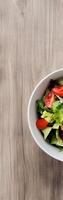 Fresh salad in a white bowl on wood grain surface with vertical negative space above for text photo