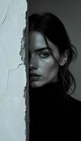 A woman in a black turtle neck peeking out from behind a wall photo