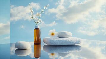 Tranquil still life with serene blue sky background featuring stone objects, white flower, and brown bottle reflected on a glass surface. Spa accessory composition set in spa hotel photo