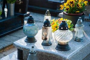 Peaceful cemetery scene with glass lanterns and vibrant flowers on a granite tombstone illuminated by sunlight photo