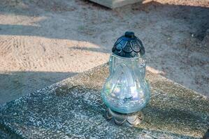 Elegant glass candle lantern with intricate design on stone surface in sunlit outdoor cemetery setting creates a serene and reflective atmosphere photo