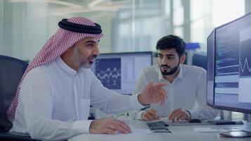 Middle-eastern adult males collaborate on business strategy in modern office setting with computers and digital analytics display. Mentor worker photo
