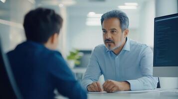 Mature caucasian male discussing computer programming with a young caucasian male in a modern office setting featuring computers and plants. Mentor worker photo