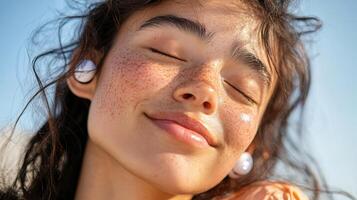 Young caucasian female with freckles enjoying the sun, smiling with closed eyes, wearing wireless earbuds, embodies summer relaxation photo