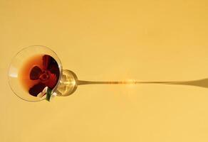 Close-up of a martini glass on a yellow background. View from above. An elegant goblet with a red alcoholic sparkling drink decorated with lime zest. Sunlight. photo