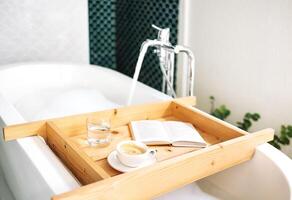 wooden tray is attached to a bathtub filled with hot fragrant water with fluffy foam photo