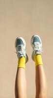 Stylish legs in vibrant yellow socks and trendy blue sneakers are raised against a soft beige background, showcasing a playful and energetic fashion statement with a modern aesthetic photo