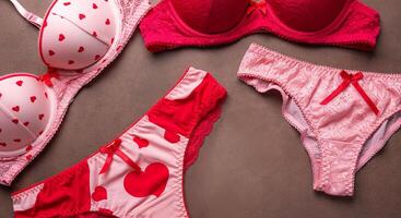 Lingerie set featuring a red bra with heart patterns and matching panties, elegantly arranged on a textured surface, showcasing vibrant colors and playful design elements photo