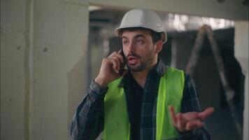 irritado caucasiano homem construtor Falando ligar Móvel telefone brigar dentro construção capataz contratante eletricista masculino comunicando Smartphone inspetor faz-tudo cara discutindo problema trabalhos dificuldade video
