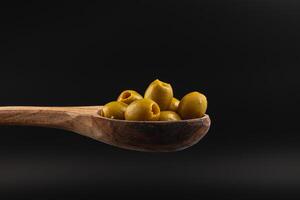 Small green olives placed on a wooden spoon against a dark background photo