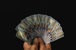 Hands show a fan of hundred-dollar bills on black photo