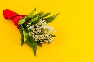 Bouquet of lily-of-the-valley with red ribbon on yellow backdrop photo
