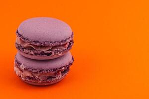 Delicious purple macarons on vibrant orange background photo