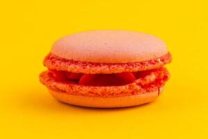 Bright orange macaron on vibrant yellow background photo