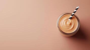 glass jar with a black and white striped straw. The jar is filled with a brown smoothie or milkshake. The background is a light brown color. photo
