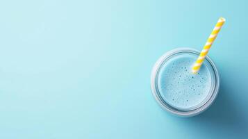 glass jar with yellow and white striped straw. The jar is filled with a blue smoothie or milkshake. The background is a light blue color photo