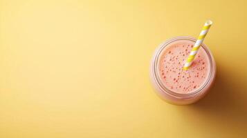 glass jar with a yellow and white striped straw. The jar is filled with a orange smoothie or milkshake. The background is a light yellow color photo