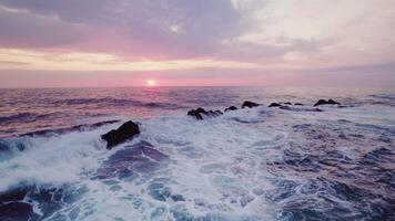 A bird's-eye view of the sea at sunset. Foam waves wash the stone reefs on the shore. Drone - Scene 6 photo