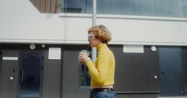 A modern young woman with glasses drinks a cocktail from a disposable glass with a straw while walking along the street of a modern city photo