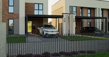 A man in casual clothes disconnects charging from an electric car parked in front of a stylish cottage. A sunny day photo
