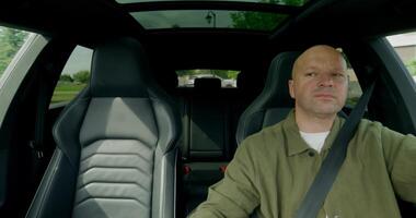 The man is driving the car, he is wearing a seat belt. Front view photo