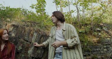 Two friends are smiling and talking standing near a ruined historical building. They smoke photo
