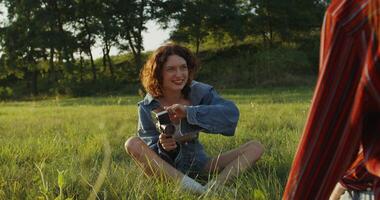 Two young women are photographed with a camera in the tall grass in a field. photo