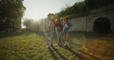 Three young friends look into the camera with a calm look standing near the ruins of a historic building. The fortress walls are overgrown with vegetation. photo