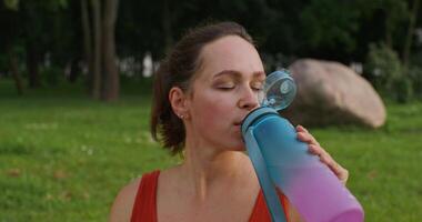 A woman is resting after sports in a city park. She drinks water from a bottle. Close-up of her face photo