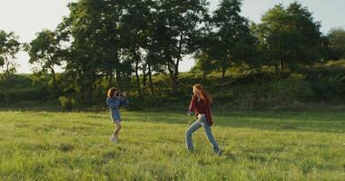 Two young women are filming a on camera standing in a field on a sunny summer day. The model is dancing and spinning around herself photo