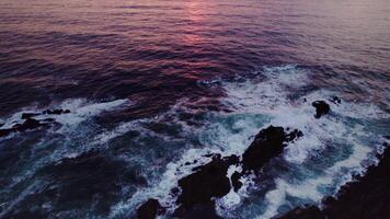 A bird's-eye view of the sea at sunset. Foam waves wash the stone reefs on the shore. Drone - Scene 2 photo