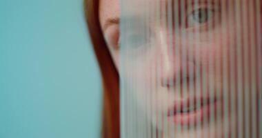 A red-haired woman with freckles is smiling at the camera while standing on a studio background. She hides behind plexiglass photo