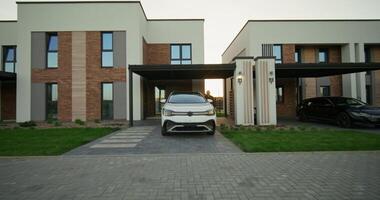 The man opens the car and sits in the driver's seat. Daylight. The car is parked near a stylish cottage photo
