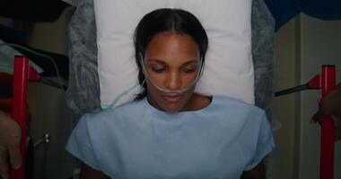 A woman with a breathing tube in her nose is lying on a gurney, top view. She is being driven down the hospital corridor photo